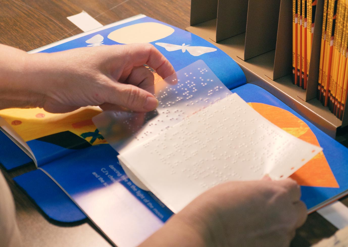 Hands affixing a braille label to a print storybook