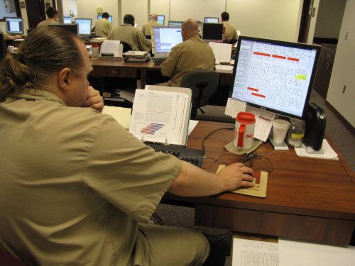 Overlooking the shoulder of a man using a computer to transcribe braille. Other transcribers can be seen at other workstations in the background.